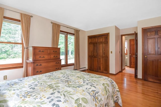 bedroom with a baseboard heating unit, a closet, and light wood-type flooring