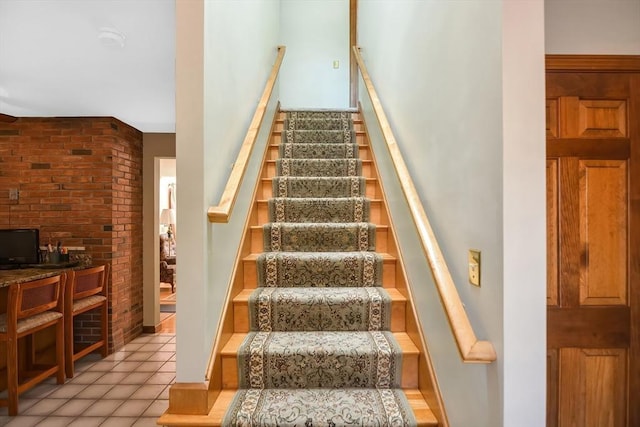 stairs with tile patterned flooring and brick wall