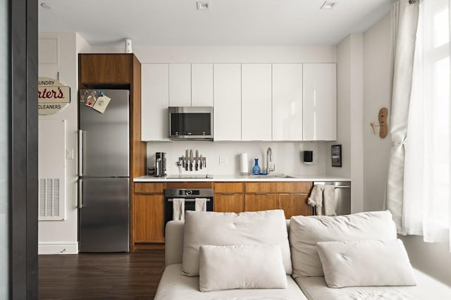 kitchen featuring a sink, open floor plan, white cabinetry, appliances with stainless steel finishes, and light countertops