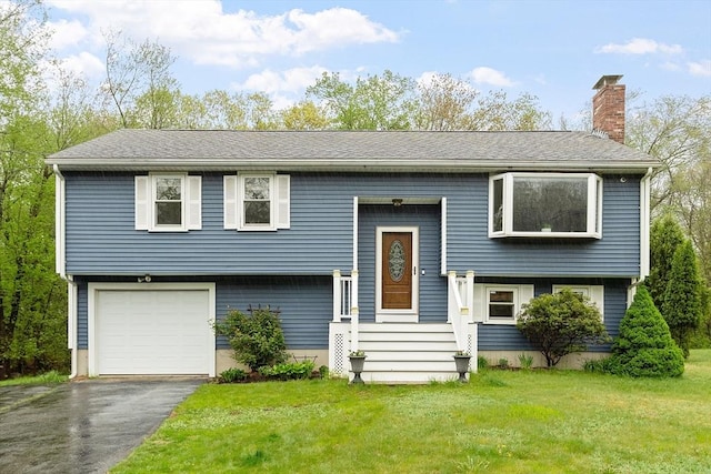 raised ranch with a chimney, a front lawn, driveway, and a garage