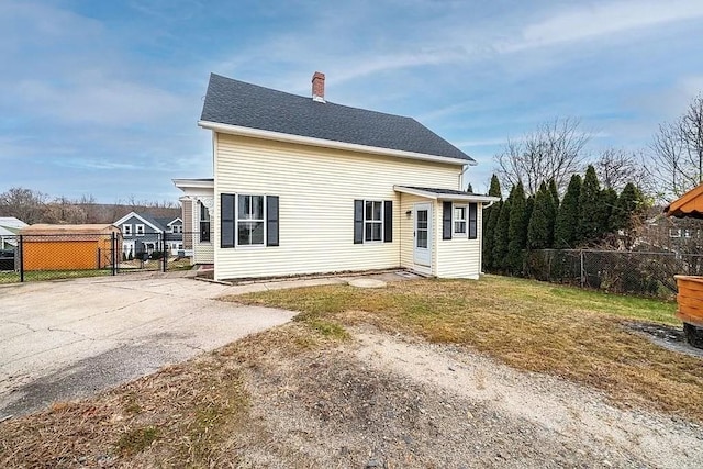 rear view of house featuring roof with shingles, a yard, a chimney, and fence