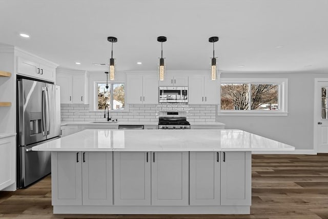 kitchen with a center island, light stone countertops, decorative light fixtures, white cabinetry, and stainless steel appliances