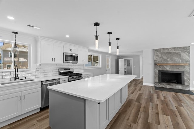 kitchen with stainless steel appliances, sink, decorative light fixtures, a center island, and white cabinetry