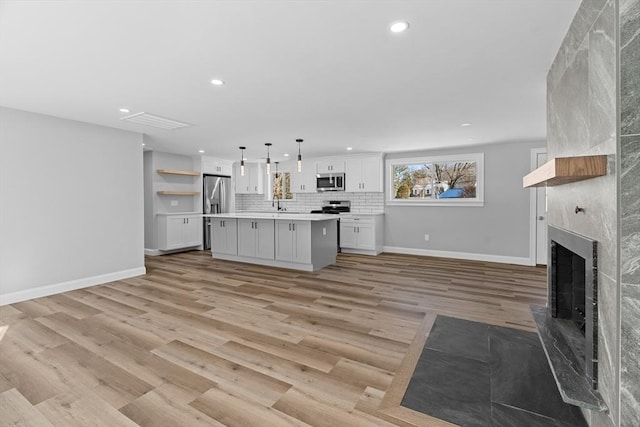 kitchen featuring white cabinetry, stainless steel appliances, pendant lighting, a fireplace, and a kitchen island