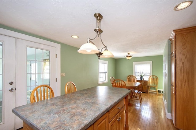 kitchen featuring light wood-type flooring, a kitchen island, french doors, and decorative light fixtures