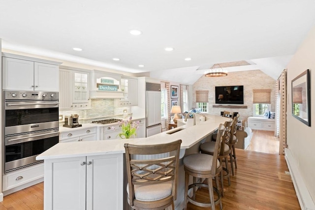kitchen featuring light wood-style floors, a breakfast bar area, stainless steel double oven, vaulted ceiling, and paneled built in fridge