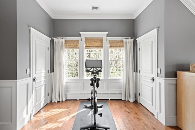 exercise area with crown molding, visible vents, light wood-style flooring, and a decorative wall
