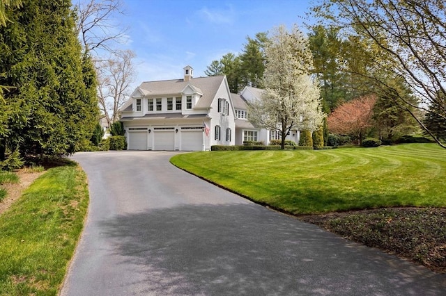 view of front of home featuring a chimney, an attached garage, a front yard, and aphalt driveway
