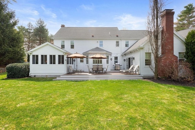 rear view of property with a lawn, outdoor dining space, a chimney, and a deck