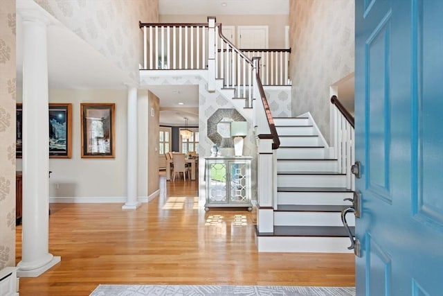 foyer entrance with ornate columns, wood finished floors, stairway, and a towering ceiling