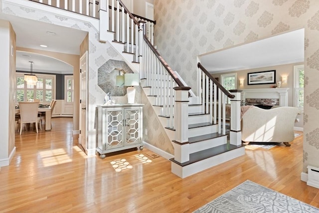 stairway with arched walkways, wallpapered walls, a healthy amount of sunlight, and wood finished floors