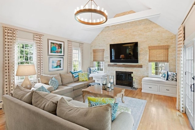 living room with a fireplace, a chandelier, vaulted ceiling with beams, and light wood-style floors