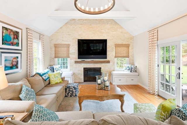 living room featuring lofted ceiling with beams, light wood finished floors, a fireplace, a chandelier, and baseboards