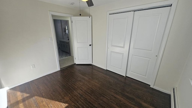 unfurnished bedroom with baseboard heating, baseboards, dark wood finished floors, and a closet