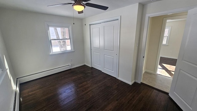 unfurnished bedroom featuring a baseboard heating unit, a closet, dark wood finished floors, and baseboards