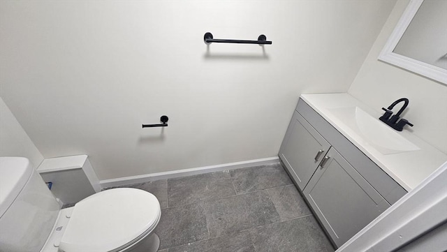 half bath with baseboards, vanity, and toilet