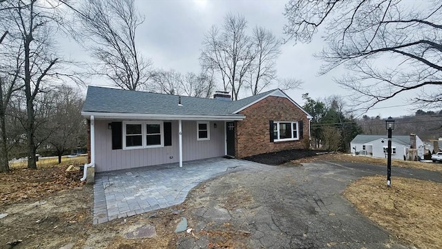 view of front of home with driveway, brick siding, a chimney, and a shingled roof