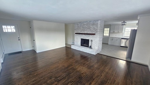 unfurnished living room featuring a brick fireplace, baseboards, and dark wood finished floors