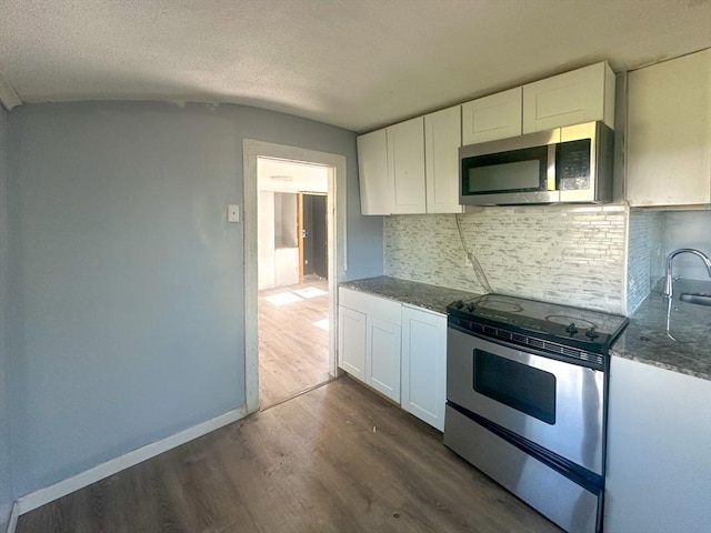 kitchen with white cabinets, dark wood finished floors, dark stone countertops, stainless steel appliances, and tasteful backsplash