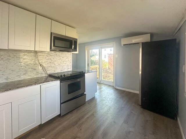 kitchen with appliances with stainless steel finishes, an AC wall unit, dark wood finished floors, white cabinetry, and tasteful backsplash