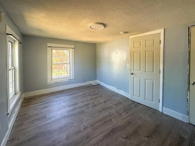 unfurnished room with dark wood-type flooring, a textured ceiling, and baseboards
