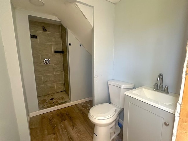 full bath with vanity, wood finished floors, toilet, baseboards, and a tile shower
