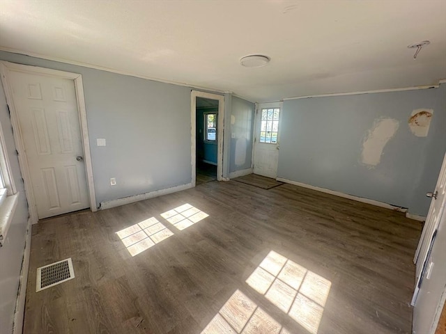 empty room featuring visible vents, ornamental molding, baseboards, and wood finished floors