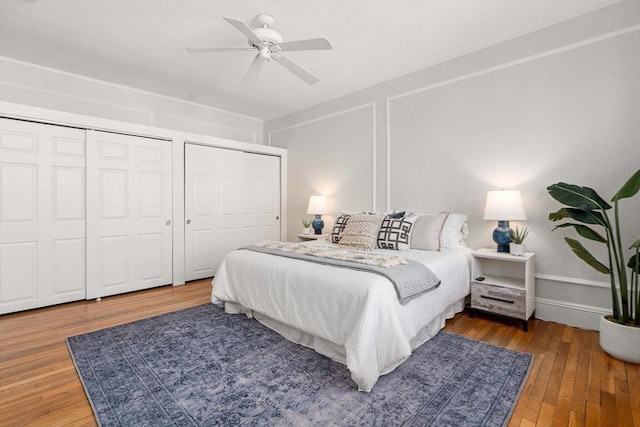 bedroom with hardwood / wood-style floors, multiple closets, and ceiling fan