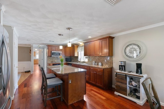 kitchen with a kitchen bar, appliances with stainless steel finishes, a sink, light stone counters, and ornamental molding