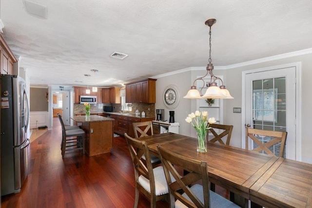 dining room featuring dark wood finished floors, ornamental molding, a healthy amount of sunlight, and visible vents
