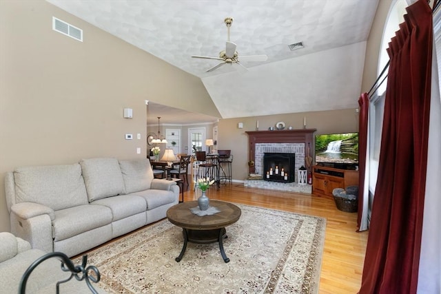 living room featuring light wood-style floors, ceiling fan, a brick fireplace, and visible vents