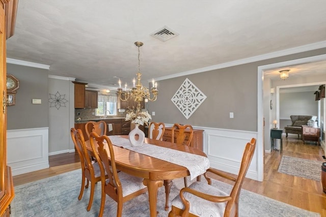 dining area with crown molding, visible vents, wainscoting, an inviting chandelier, and light wood-style floors