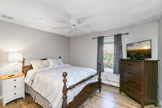 bedroom featuring baseboard heating, light wood-style floors, a ceiling fan, baseboards, and visible vents