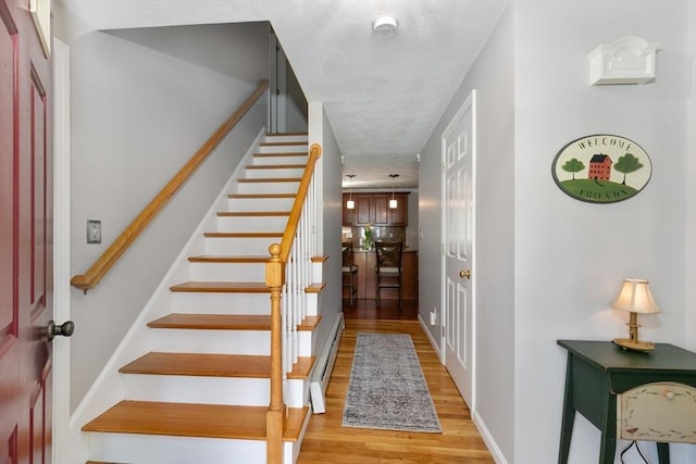 stairs with baseboard heating, baseboards, and wood finished floors