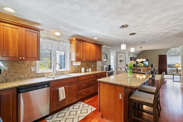 kitchen with a center island, wood finished floors, dishwasher, a sink, and light stone counters