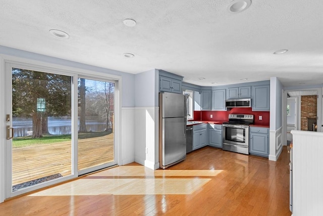 kitchen featuring light wood-style flooring, a textured ceiling, appliances with stainless steel finishes, and gray cabinetry