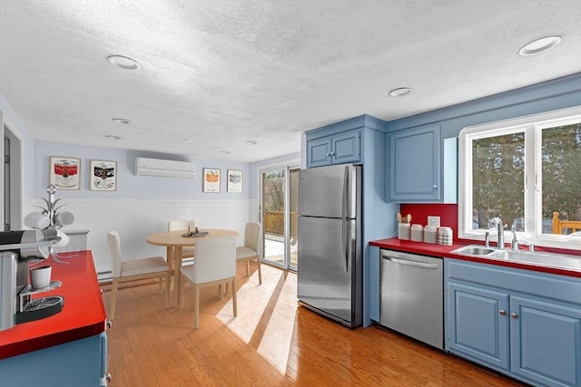 kitchen with blue cabinets, a wall mounted AC, a textured ceiling, and appliances with stainless steel finishes
