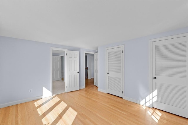 unfurnished bedroom featuring light wood-type flooring, multiple closets, and baseboards