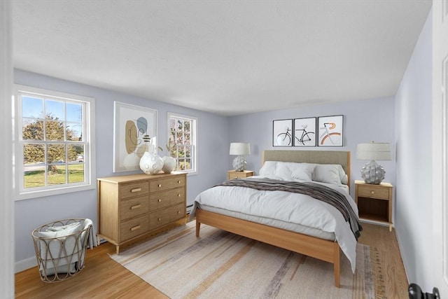 bedroom with a baseboard heating unit, baseboards, and light wood-type flooring