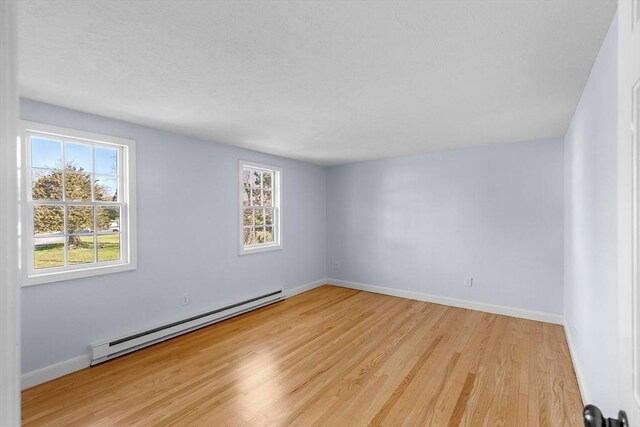 unfurnished room with baseboards, light wood-style floors, and a baseboard radiator