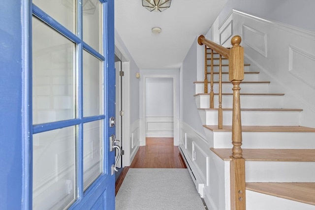 corridor with a wainscoted wall, stairs, a baseboard radiator, and a decorative wall
