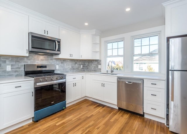 kitchen featuring white cabinetry, sink, decorative backsplash, stainless steel appliances, and light wood-type flooring