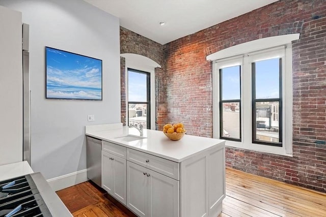 kitchen with stainless steel dishwasher, a peninsula, brick wall, hardwood / wood-style floors, and a sink