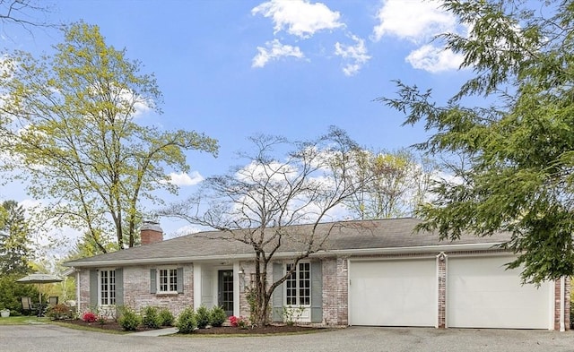single story home featuring an attached garage, a chimney, driveway, and brick siding