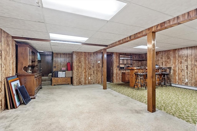 basement featuring a drop ceiling, indoor bar, wood walls, and carpet