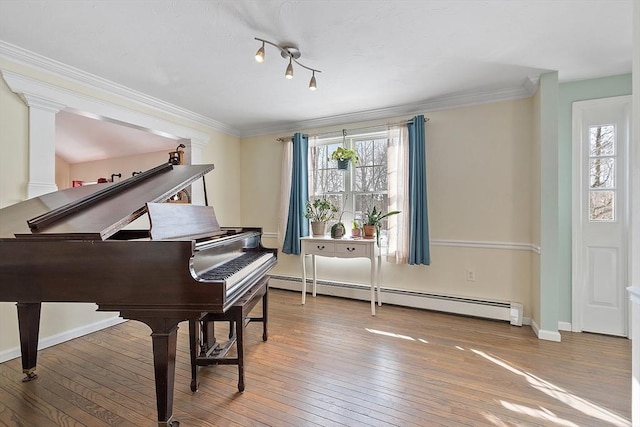 living area featuring a healthy amount of sunlight, wood-type flooring, a baseboard heating unit, and ornamental molding