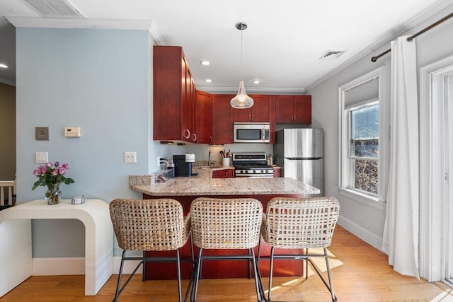 kitchen with a peninsula, crown molding, appliances with stainless steel finishes, and light wood-style flooring