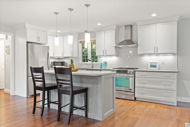 35 Orchard Rd, Milton, MA 02186 - kitchen featuring wall chimney range hood, appliances with stainless steel finishes, a breakfast bar, light countertops, and light wood-style flooring