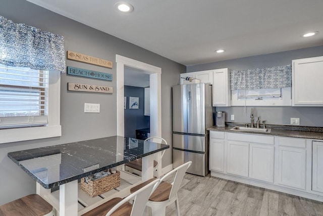 kitchen with white cabinetry, sink, a breakfast bar area, and stainless steel refrigerator