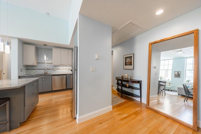 kitchen featuring dishwasher, gray cabinets, light wood finished floors, backsplash, and light stone countertops